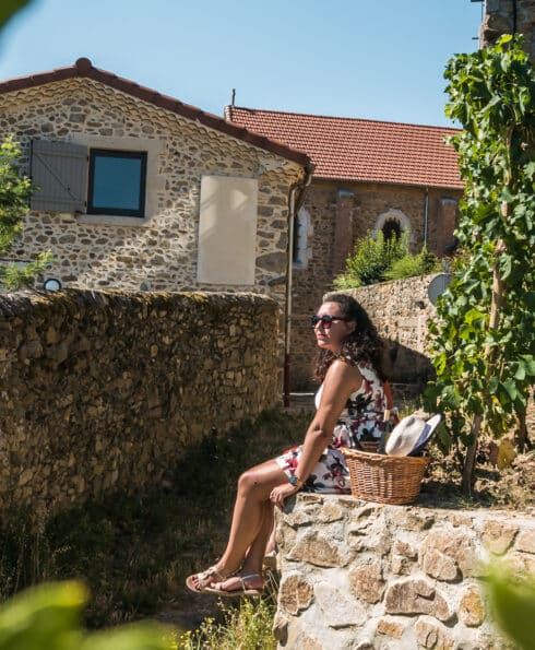 Jeune femme assise sur un muret devant des vignes et contemplant l'horizon