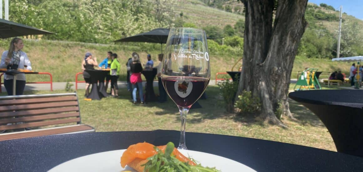 Assiette avec verre de vin rouge avec les coteaux viticoles en fond ainsi que des cyclistes