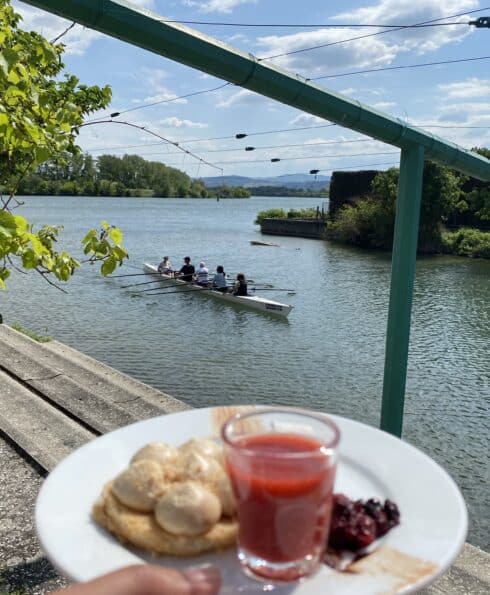 Main tenant une assiette de desserts devant un bassin de joutes où passe un aviron
