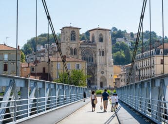 Famille de quatre personnes de dos marchant sur la passerelle de Vienne face à la cathédrale