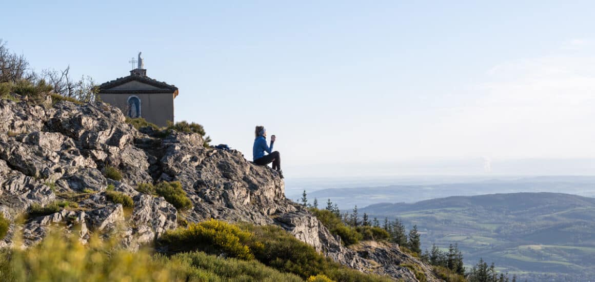 Jeune femme contemplant le panorama du Parc naturel régional du Pilat, devant une chapelle